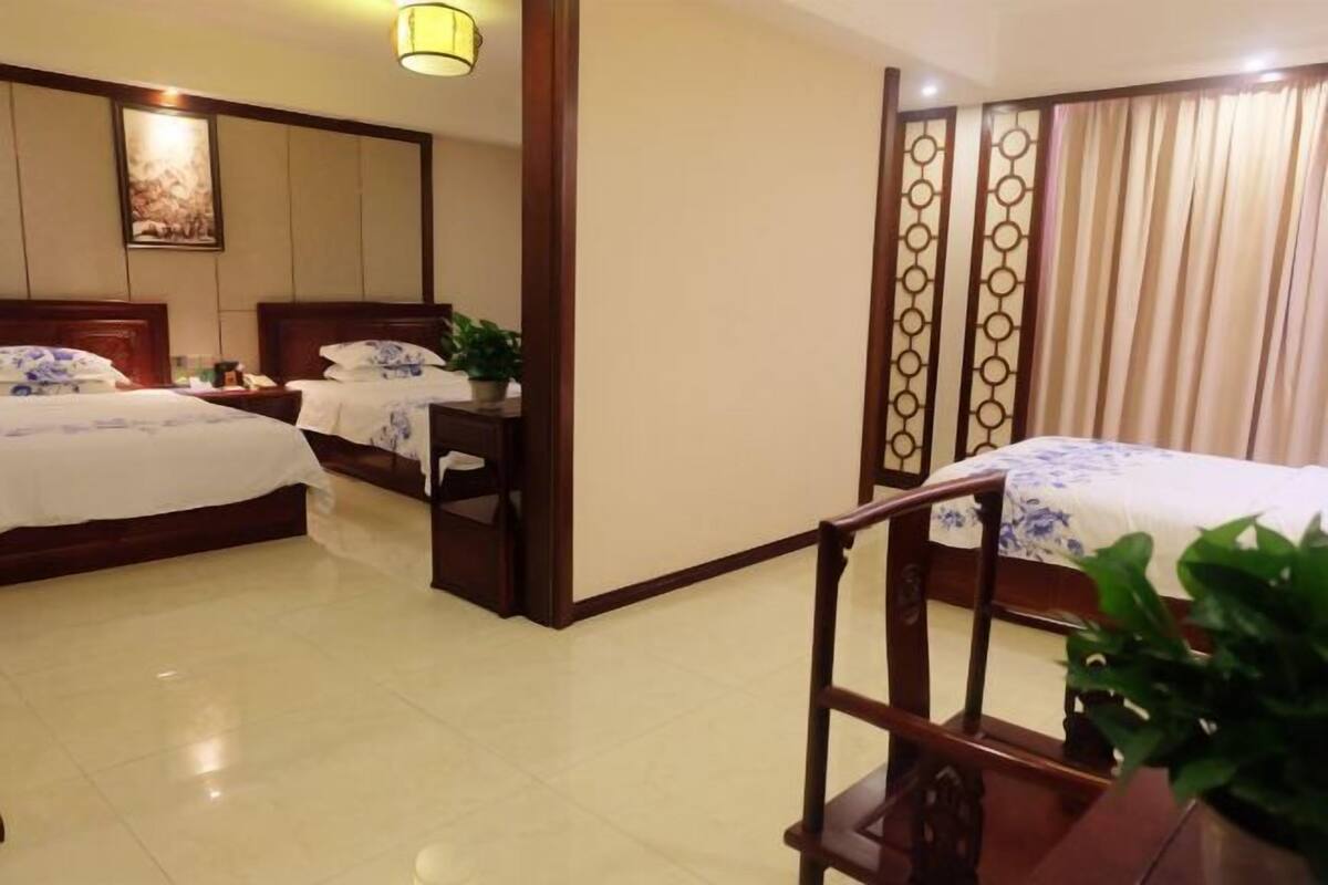 A hotel room with two beds, a desk, a chair, a potted plant, and a decorative screen.
