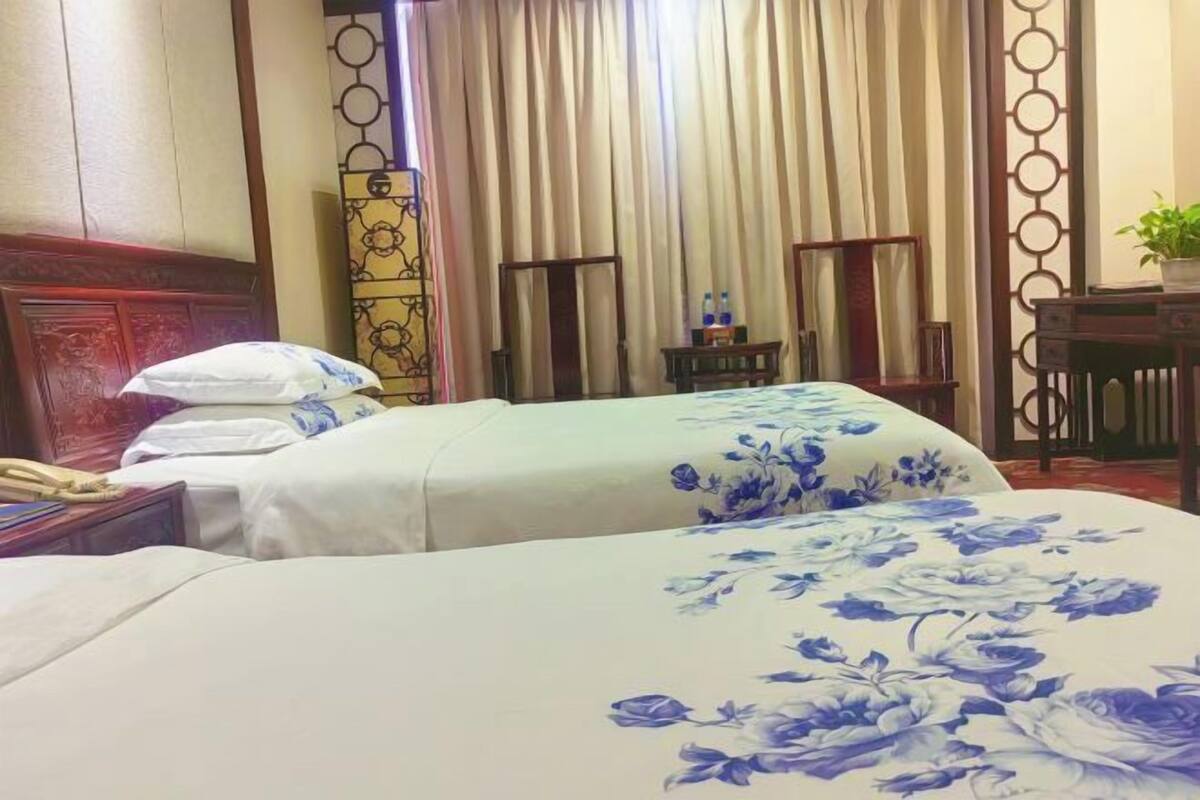 A hotel room with two beds, a wooden headboard, a small table with a plant, and a curtain divider.