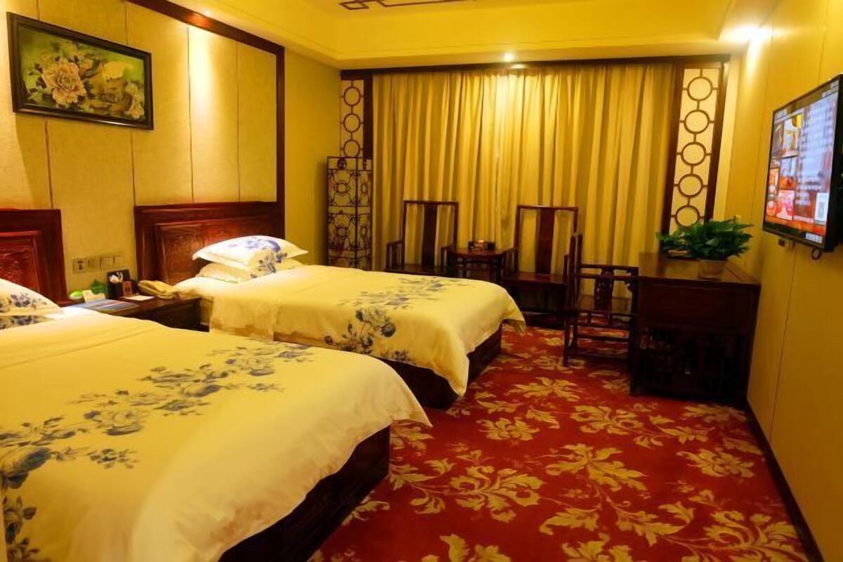 A hotel room with two beds, a red carpet, a desk, and a television.