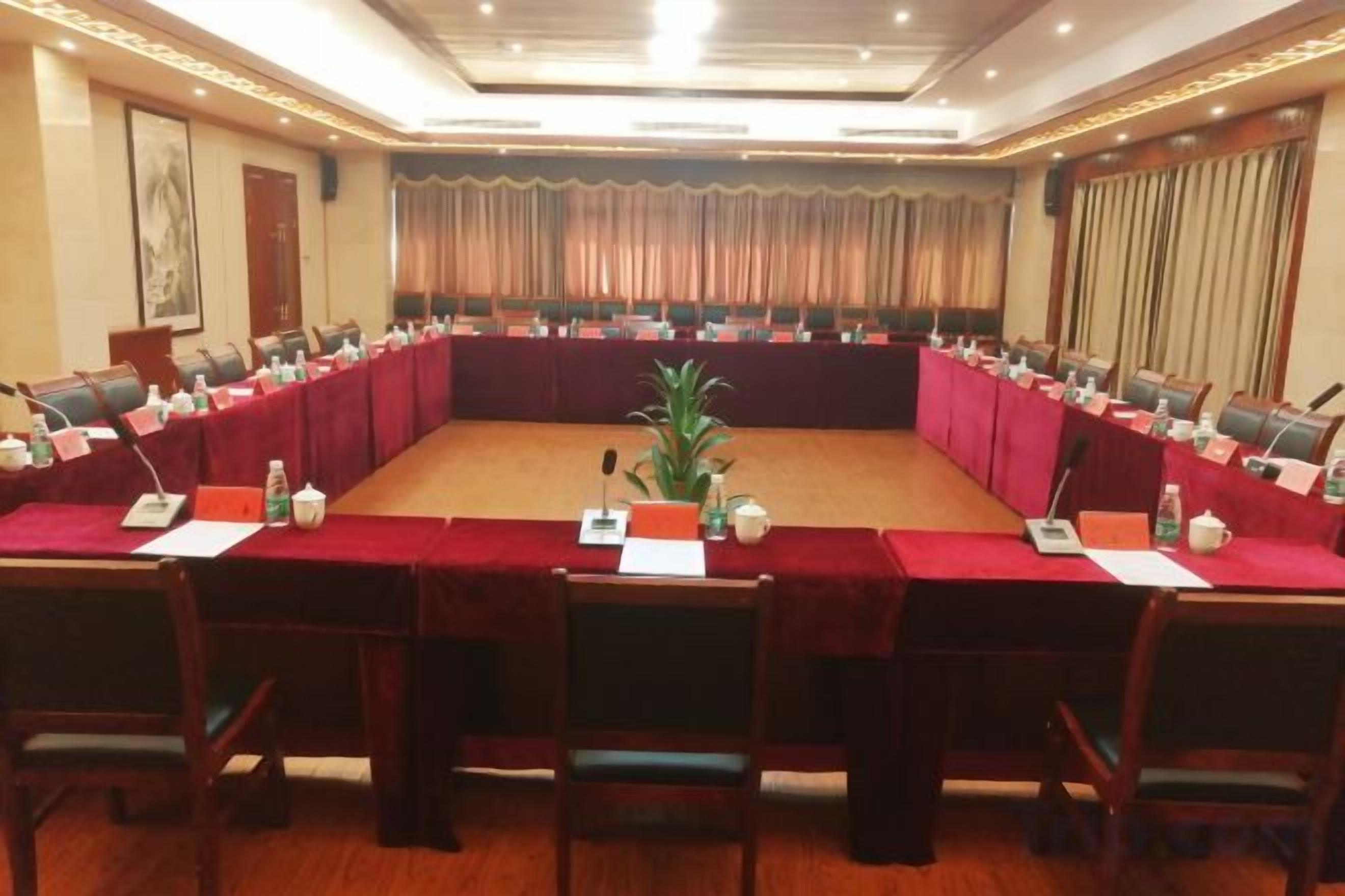 A conference room with a long table, chairs, nameplates, microphones, and a plant.