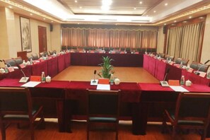 A conference room with a long table, chairs, nameplates, microphones, and a plant.