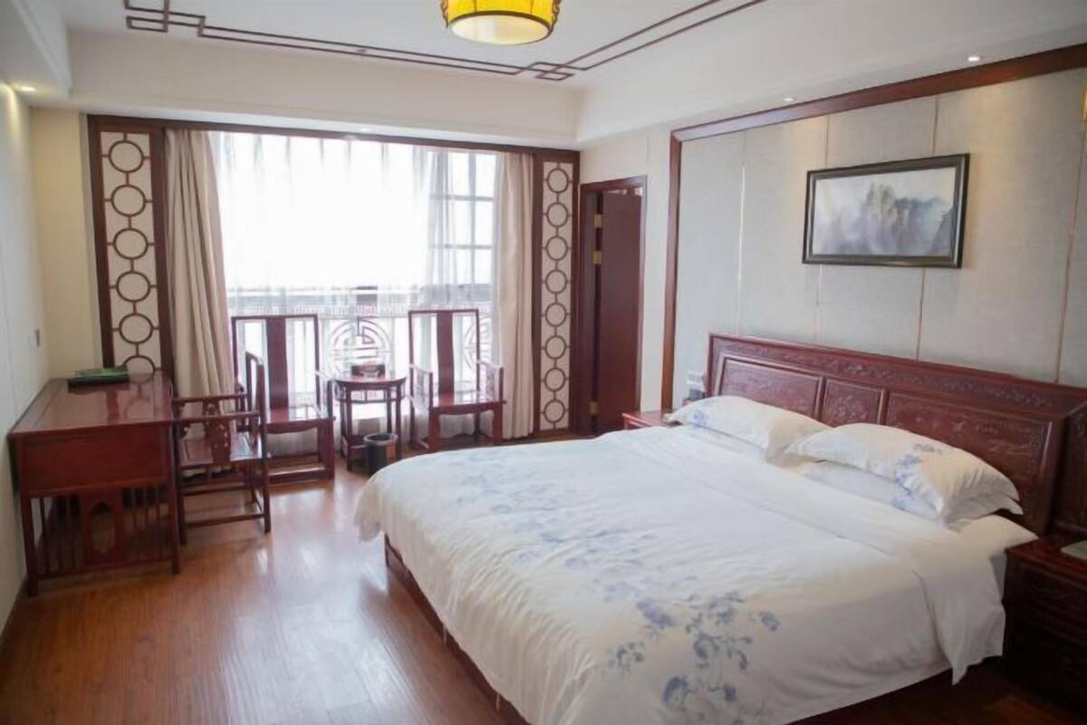 A hotel room with a large bed, a desk, a chair, and a view of the outdoors.