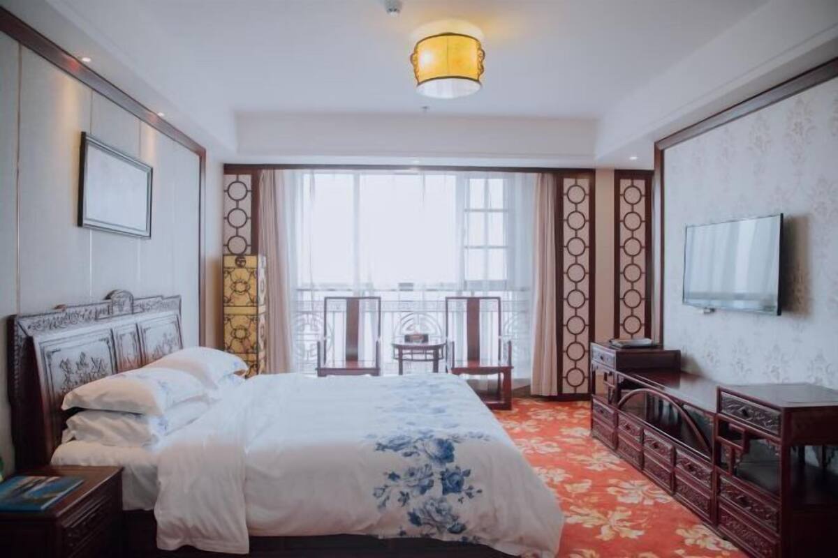 A hotel room with a bed, a TV, a desk, and a balcony with chairs.