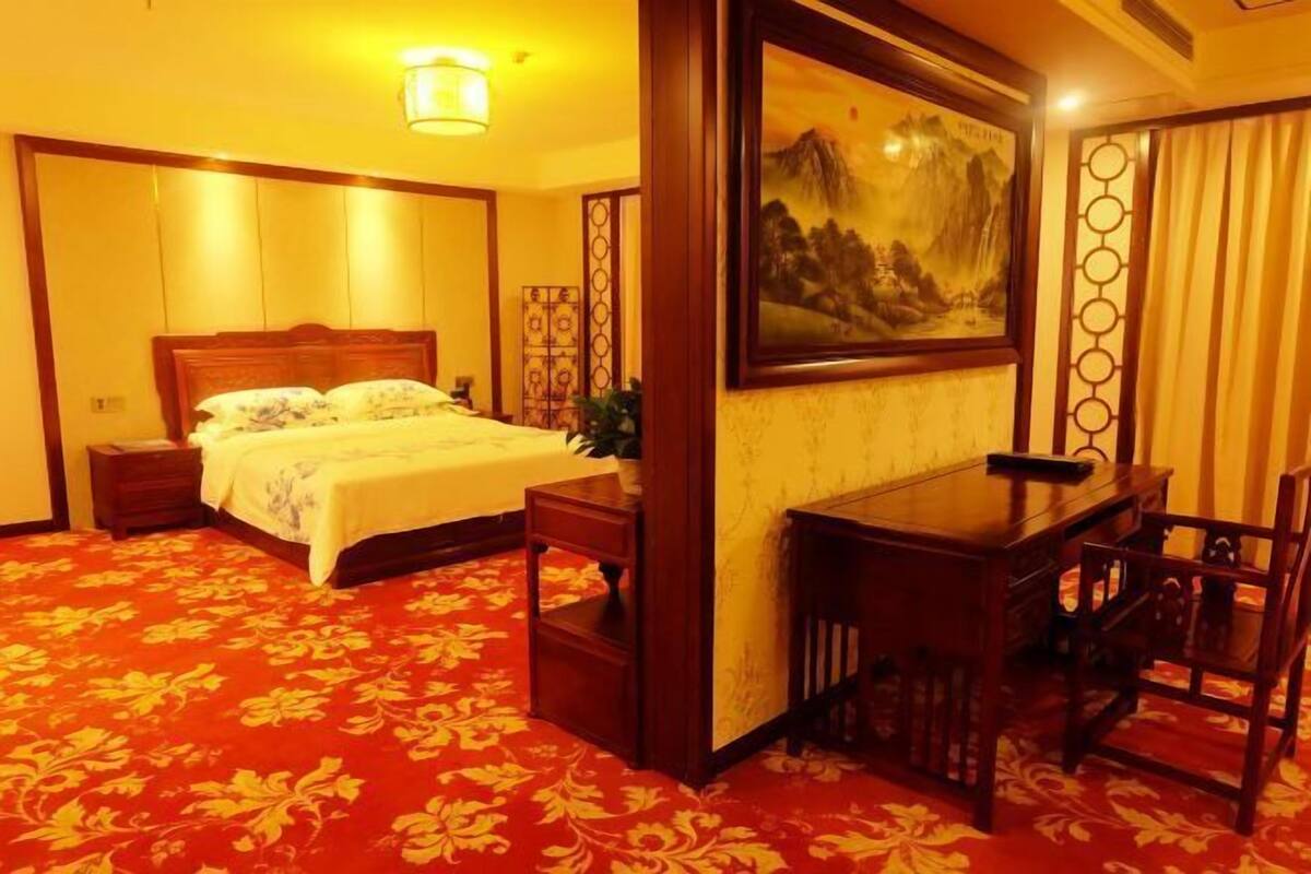 A hotel room with a bed, bedside table, and a desk with chairs.