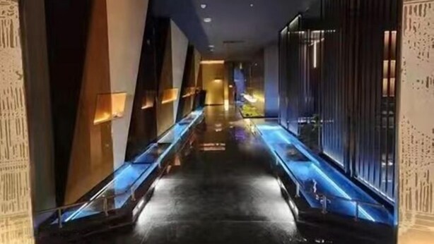 Een moderne hotelgang met een spiegelende vloer, glazen balustrades en decoratieve verlichting.