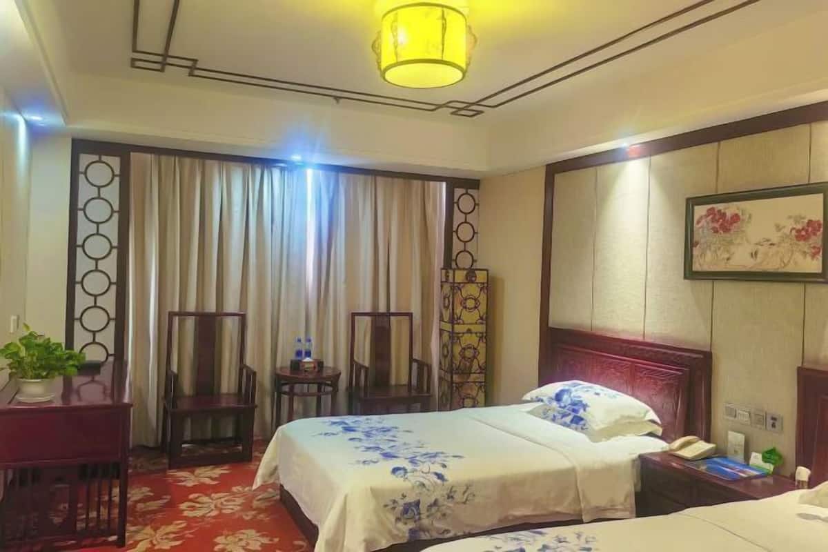 A hotel room with a bed, a desk with a chair, a lamp, a telephone, and a decorative wall piece.