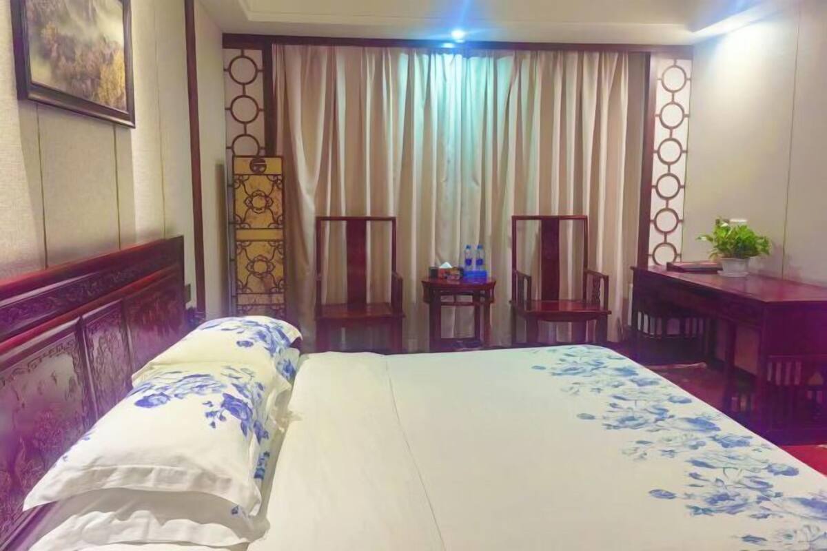 A hotel room with a bed, a desk, two chairs, a small table, and a curtain.