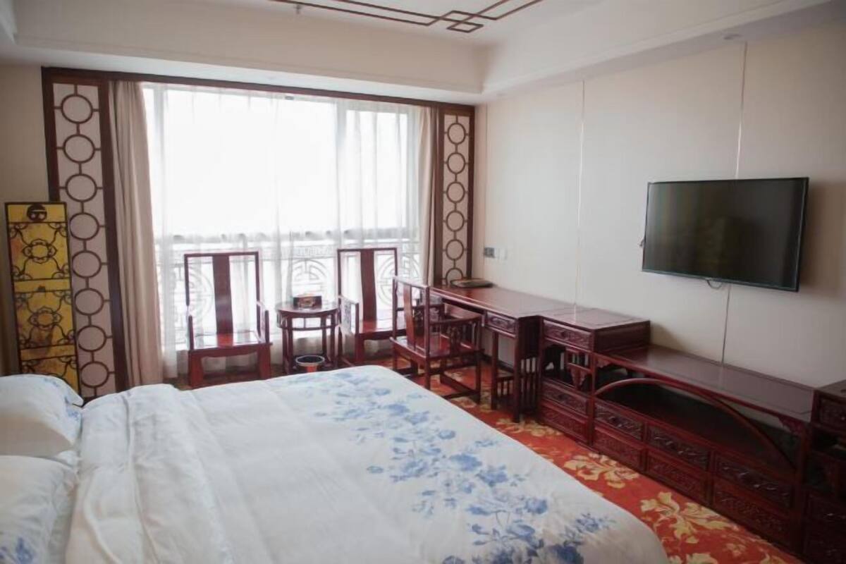A hotel room with a bed, a desk, a TV, and a balcony with a view.