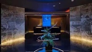 Een moderne lobby met een centraal waterkunstwerk, behang met patroon en een donker plafond.
