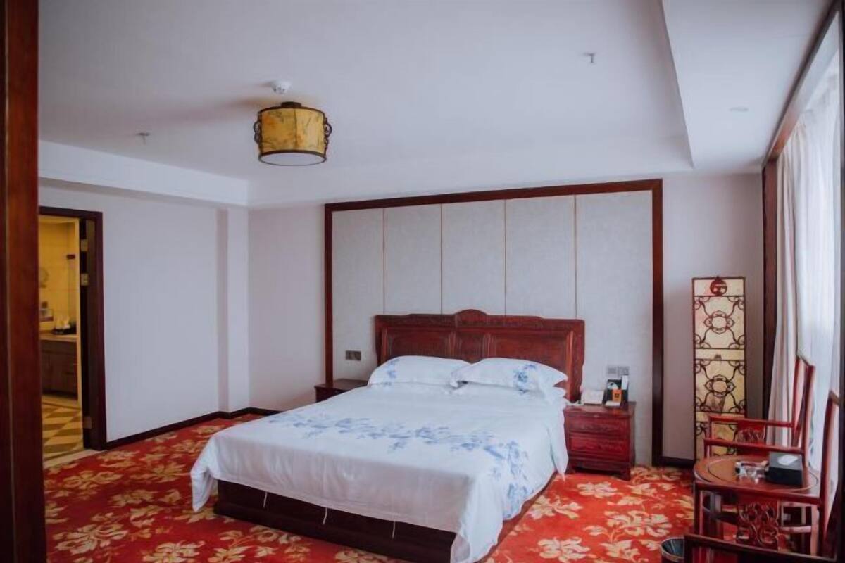 A hotel room with a bed, a nightstand, a chair, a lamp, and a decorative screen.