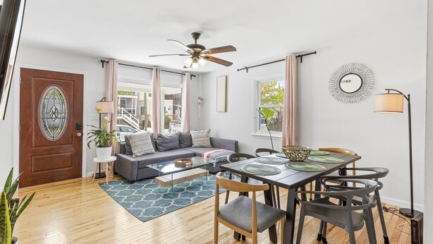 A modern living room with a sofa, dining table, chairs, and a ceiling fan.