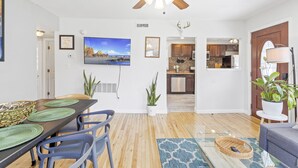 A modern living room with a dining area, a kitchen in the background, and a ceiling fan.