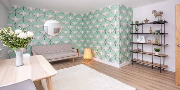 A room with a sofa, a round mirror, a wooden table, a white rug, and a wall with a green and white pattern. - James' Place at The Taff (Merthyr Tydfil)