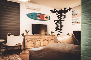 A room with a TV on a wooden cabinet, a surfboard decoration, and a unique wall art piece.