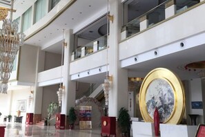 A spacious lobby with a grand chandelier, a large circular artwork, and multiple levels with glass railings.