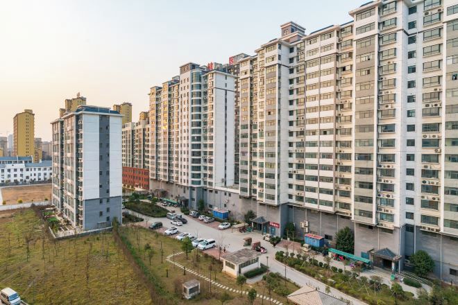 Un immeuble résidentiel de grande hauteur, doté de nombreux étages, de balcons et d’un espace de stationnement à l’avant.
