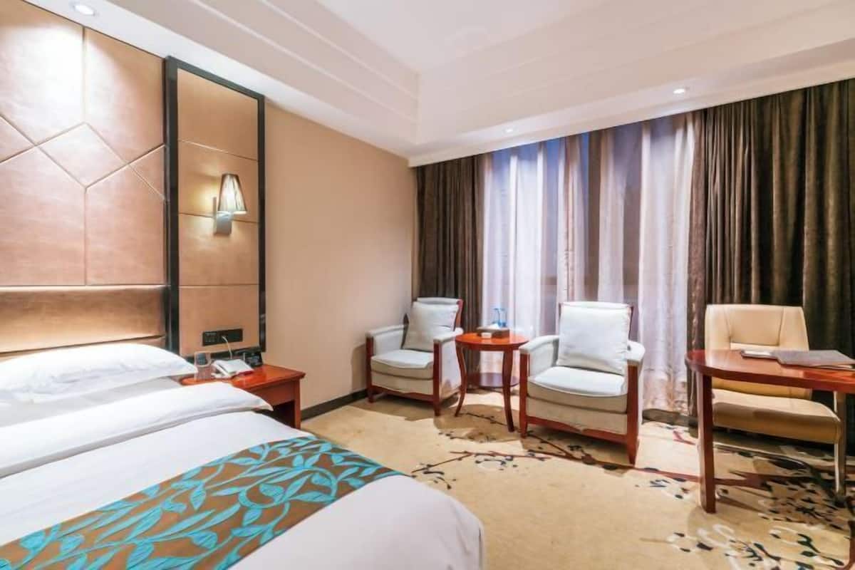 A hotel room with a large bed, two armchairs, a small table, and a desk.