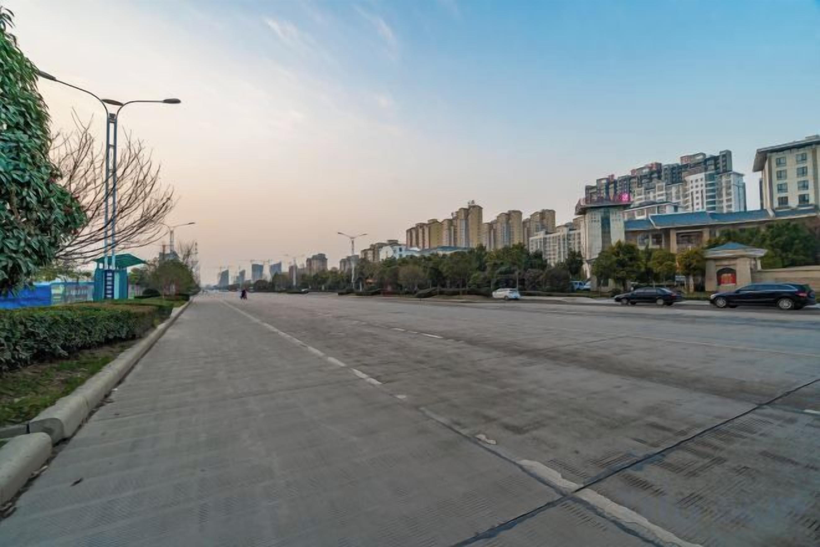 Una carretera ancha y vacía con edificios a la derecha y cielo despejado.