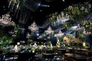 Un espacio interior con mesas dispuestas para comer, decorado con follaje y arreglos florales colgantes.