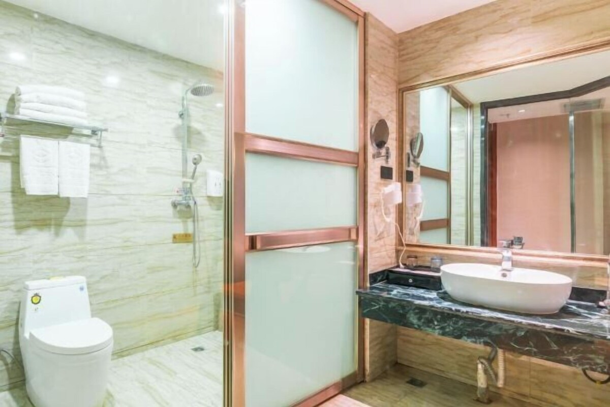 Casa de banho com sanita, chuveiro envolto em vidro, lavatório com bancada de mármore e um espelho grande.