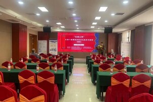 Un salón de conferencias con filas de mesas y sillas, una pantalla de presentación y un escenario.