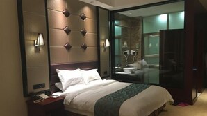 A hotel room with a large bed, a nightstand with a phone, a mirror, and a bathroom visible through a glass partition. - Suopurui International Hotel (Linying)