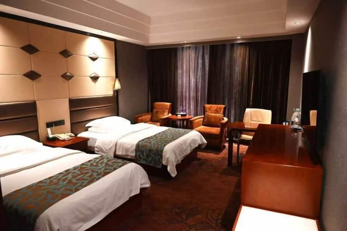 A hotel room with two beds, a desk, a chair, a TV, and a window with curtains.