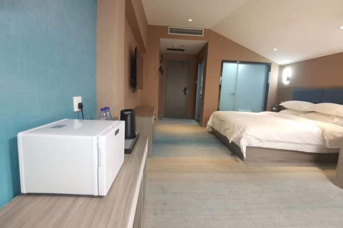 A hotel room with a bed, a desk with a computer, a TV, and a minibar.