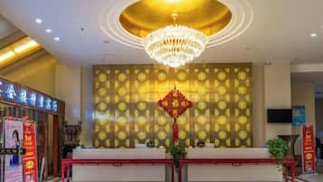 A hotel reception area with a chandelier, reception desk, patterned wall, and a red decorative element.