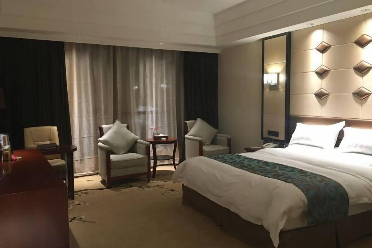 A hotel room with a bed, two armchairs, a small table, a desk, and a large mirror.
