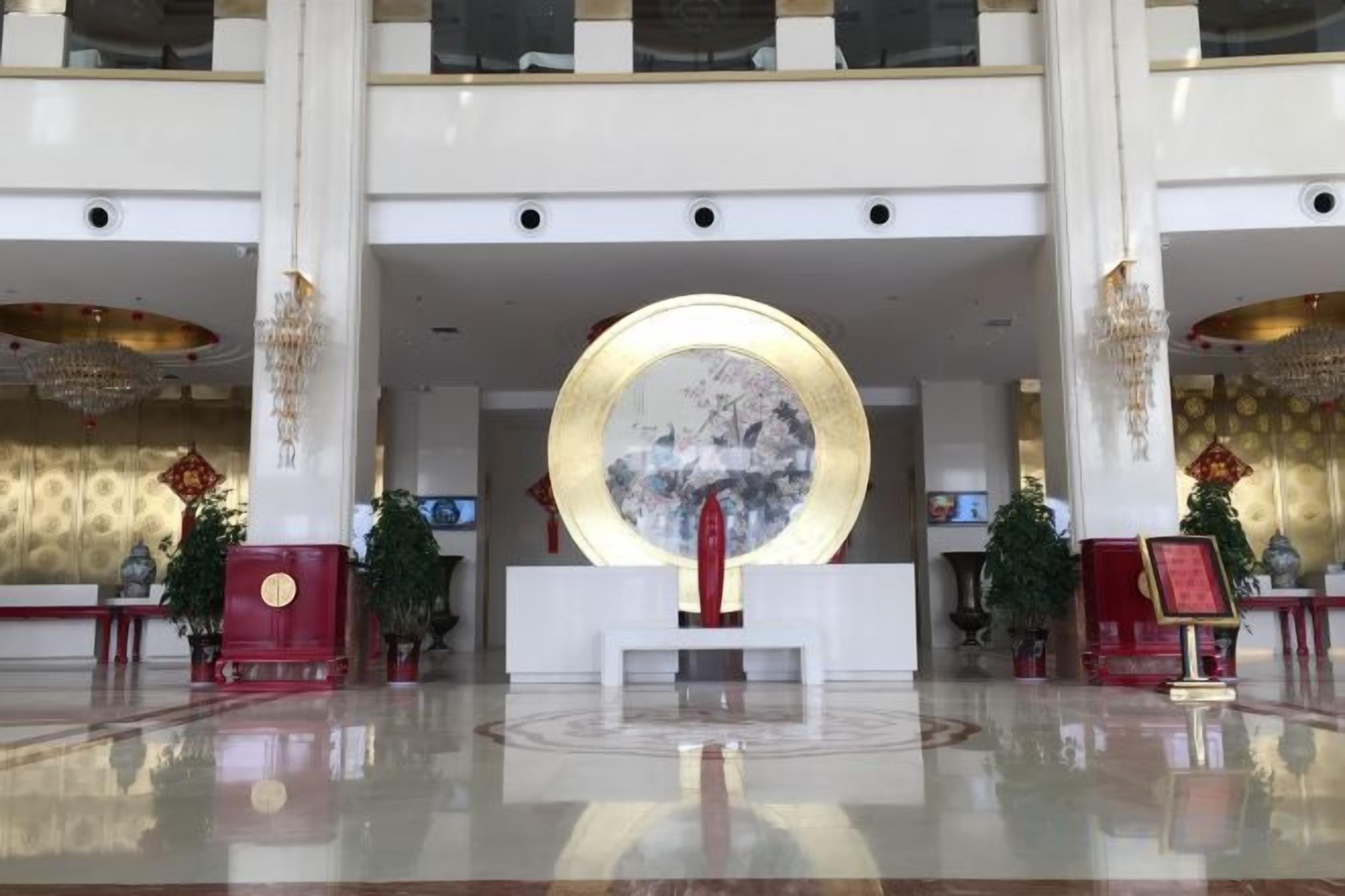 Um hall amplo com uma mesa de recepção central, grandes elementos decorativos circulares e um lustre.