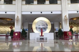 Un vestíbulo espacioso con una recepción central, grandes detalles decorativos circulares y un candelabro.