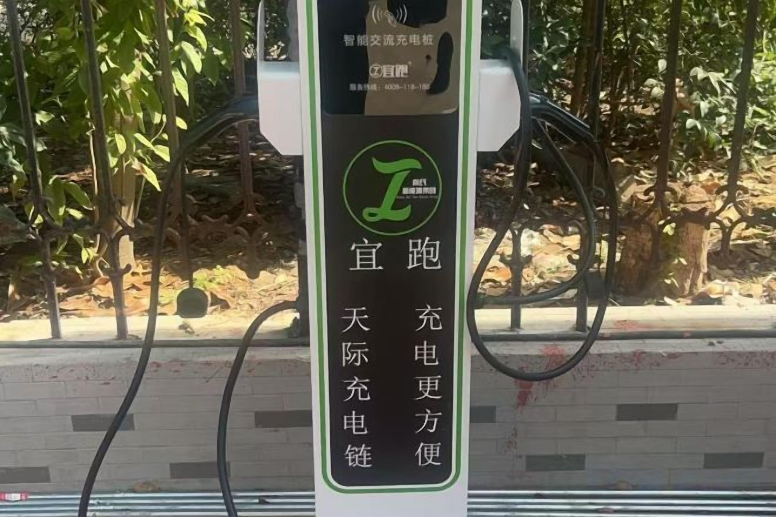 A charging station with a green logo and Chinese text, surrounded by trees.