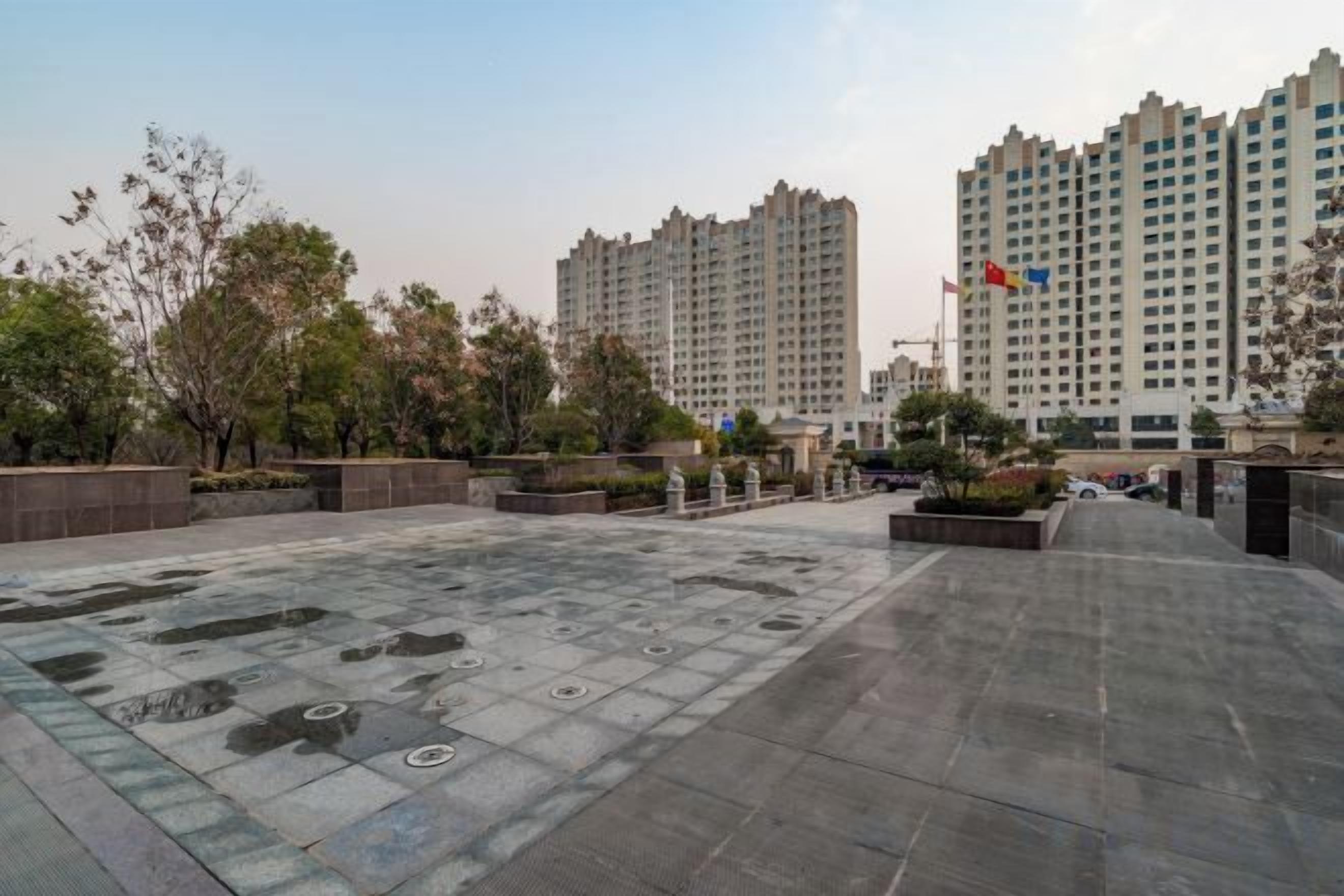 Un patio con suelo empedrado, rodeado de edificios, árboles y una bandera.