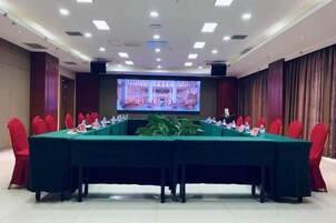 Un salón de conferencias con una larga mesa, sillas rojas, una pantalla y una planta.
