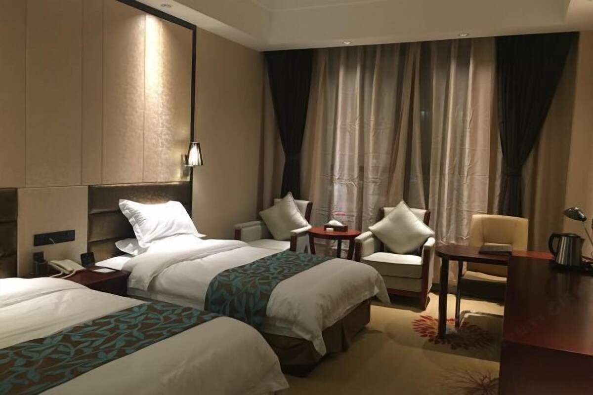 Quarto de hotel com duas camas, uma escrivaninha, uma cadeira e uma mesa pequena.