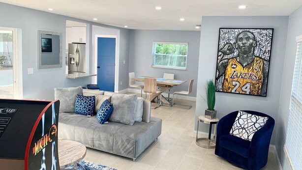 A modern living room with a grey sofa, a blue armchair, and a dining area with a wooden table and chairs. - Poolside Palms  (West Palm Beach)