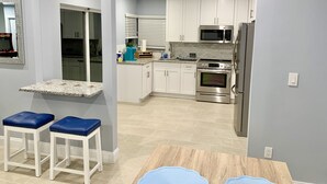 A modern kitchen with white cabinets, a microwave, oven, and a refrigerator. There are two blue stools and a small table with a blue table runner. - Poolside Palms  (West Palm Beach)