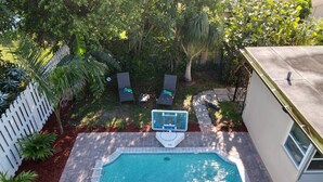 A backyard with a swimming pool, a white picket fence, and a basketball hoop. - Poolside Palms  (West Palm Beach)