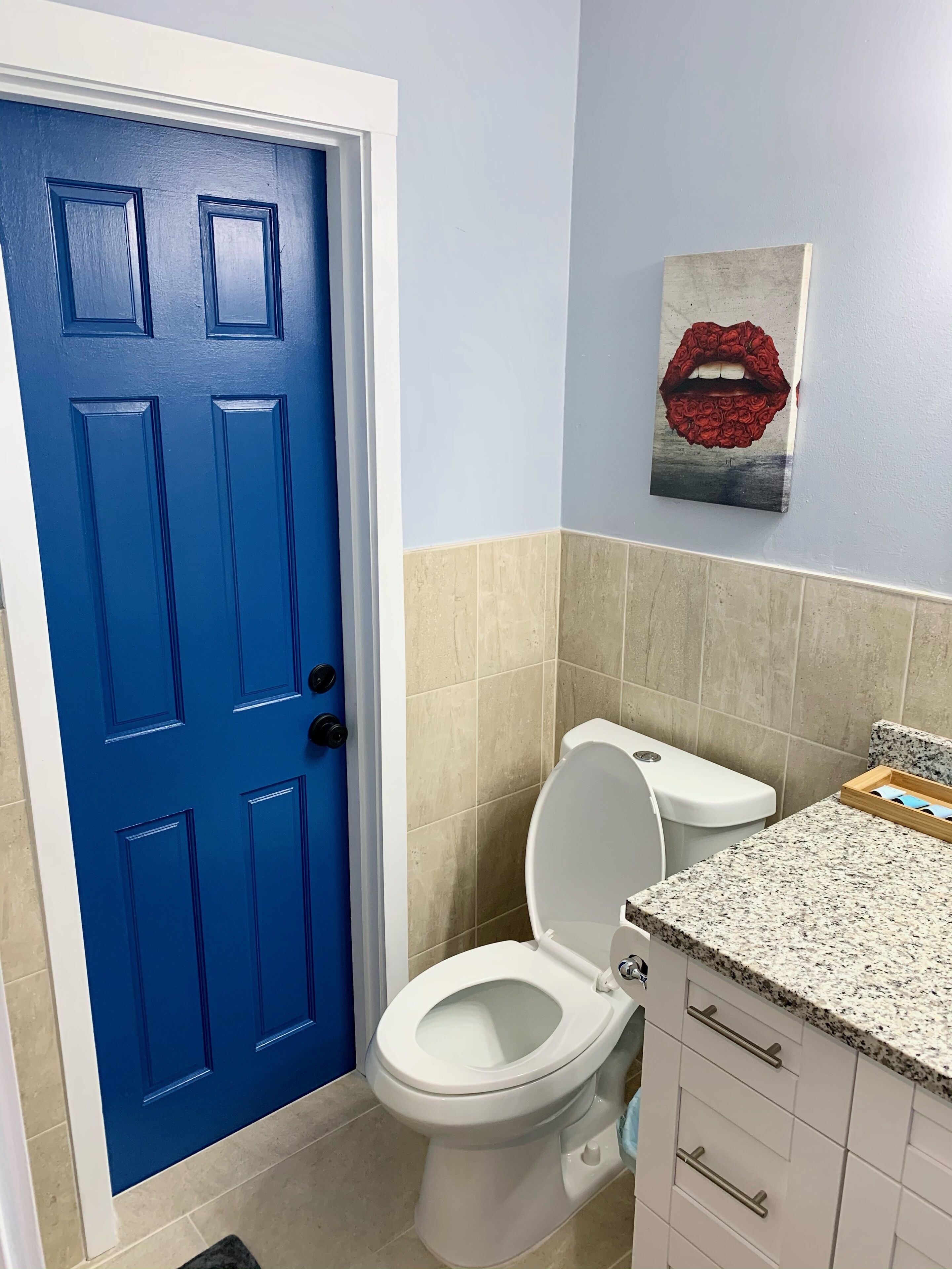 Une salle de bain avec une porte bleue, des toilettes blanches, des carreaux beiges et un comptoir en granit.