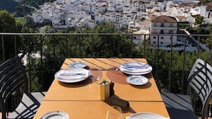 Une table à manger dressée pour quatre personnes, avec vue sur une ville et des collines en arrière-plan.