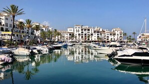 Un port de plaisance où sont amarrés des bateaux, entouré de bâtiments blancs dotés de balcons et de palmiers.