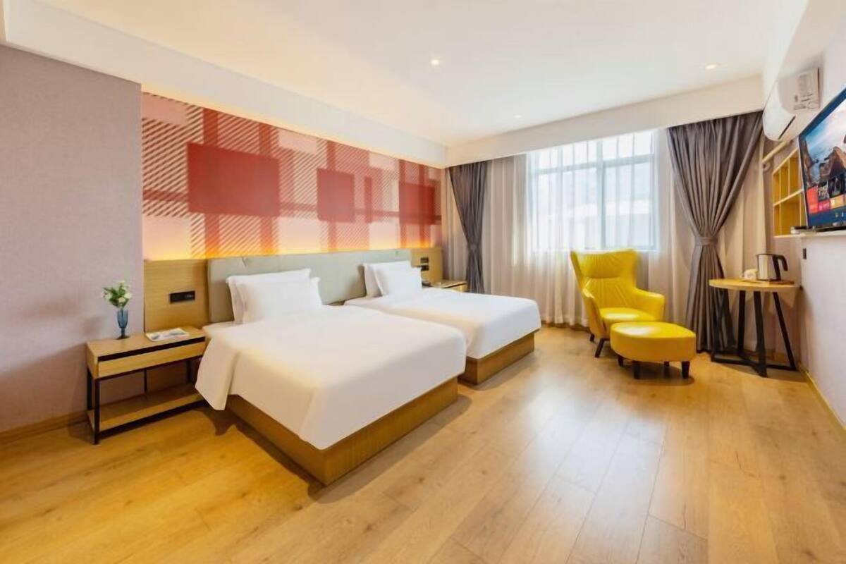 Una habitación de hotel con dos camas, un sillón amarillo, una mesita y un televisor.