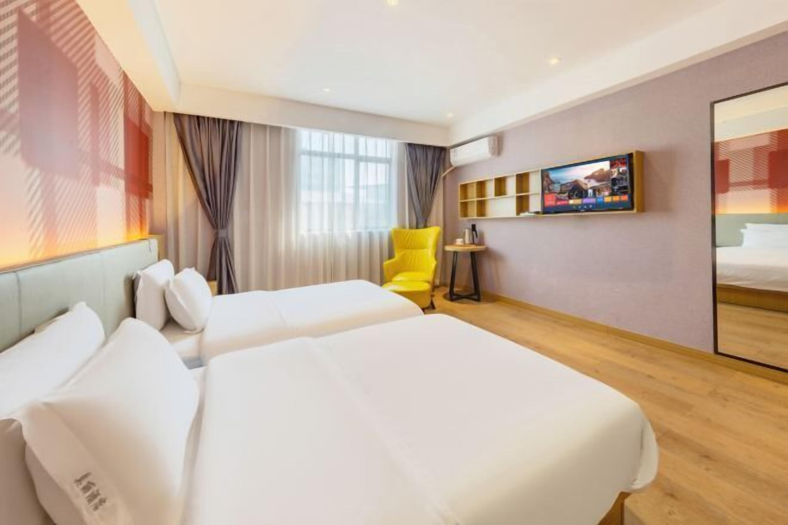 Quarto de hotel com duas camas, uma cadeira amarela, uma televisão e uma mesinha.