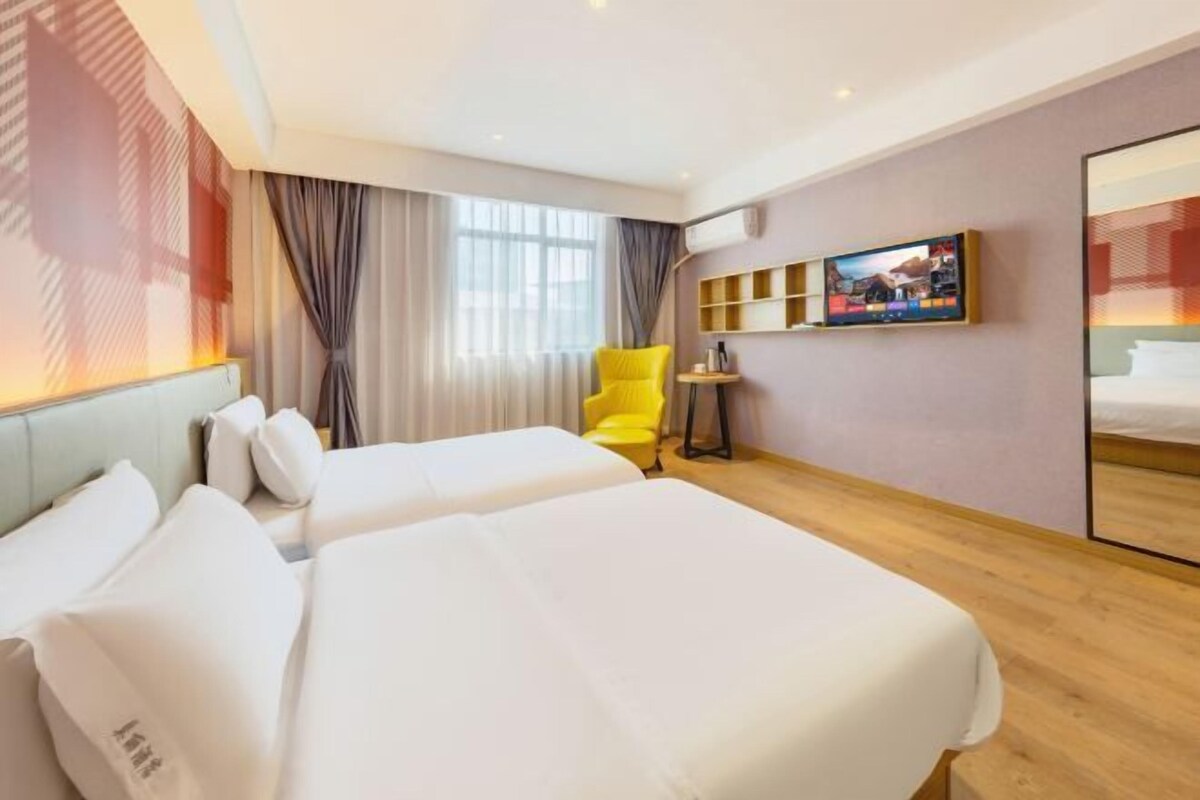 A hotel room with two beds, a yellow chair, a TV, and a small table.