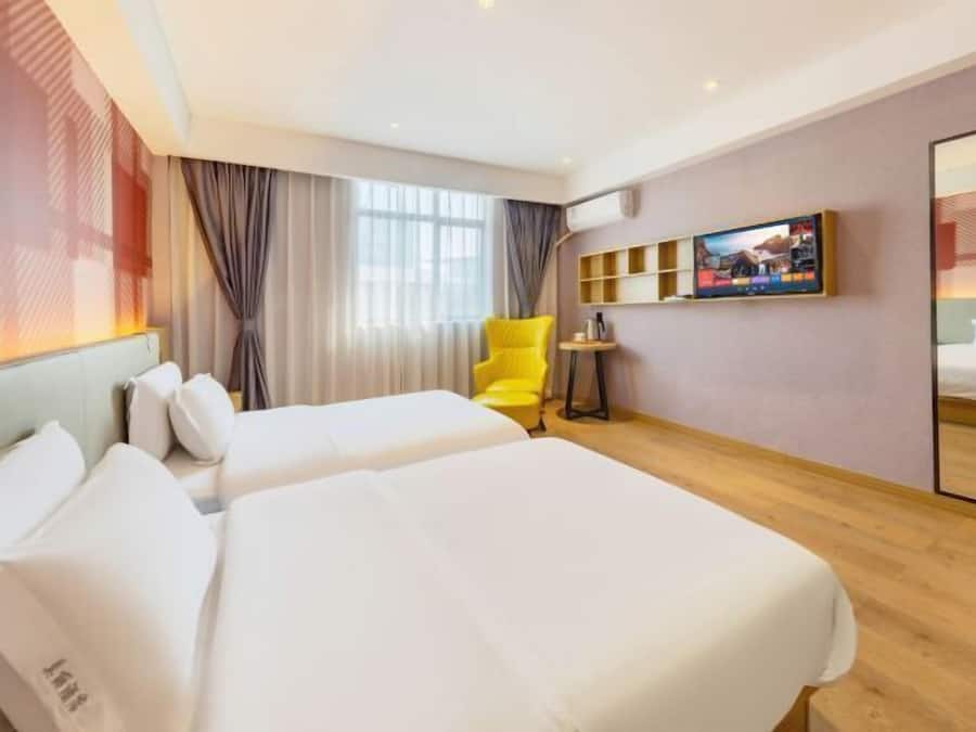 Una habitación de hotel con dos camas, una silla amarilla, un televisor y una mesita.