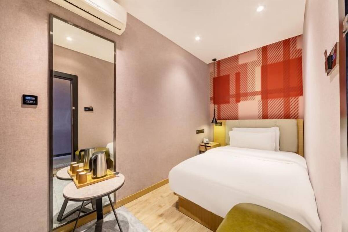 Habitación de hotel con cama, una mesita con hervidor, mesita de noche y televisor en la pared.