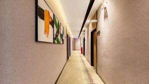 Un long couloir étroit, typique des hôtels, avec un sol recouvert de moquette et des murs ornés d’œuvres d’art abstraites.