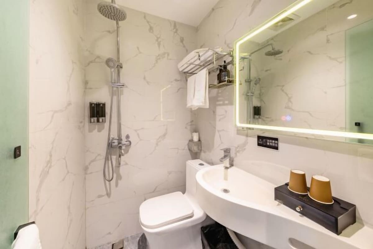 A modern bathroom with a marble wall, a white sink, a toilet, and a shower.