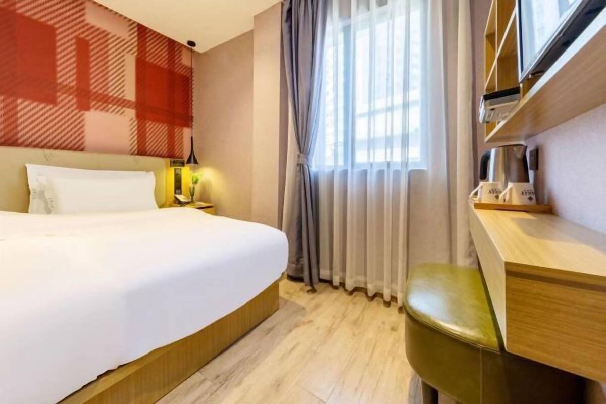 Habitación de hotel con cama, escritorio con silla, cafetera y ventana con cortinas.